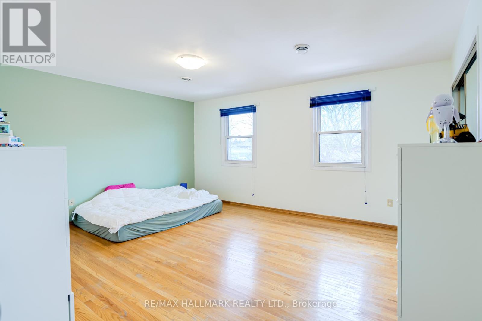 A bedroom with a bed, a window with blue blinds, and a wooden floor.