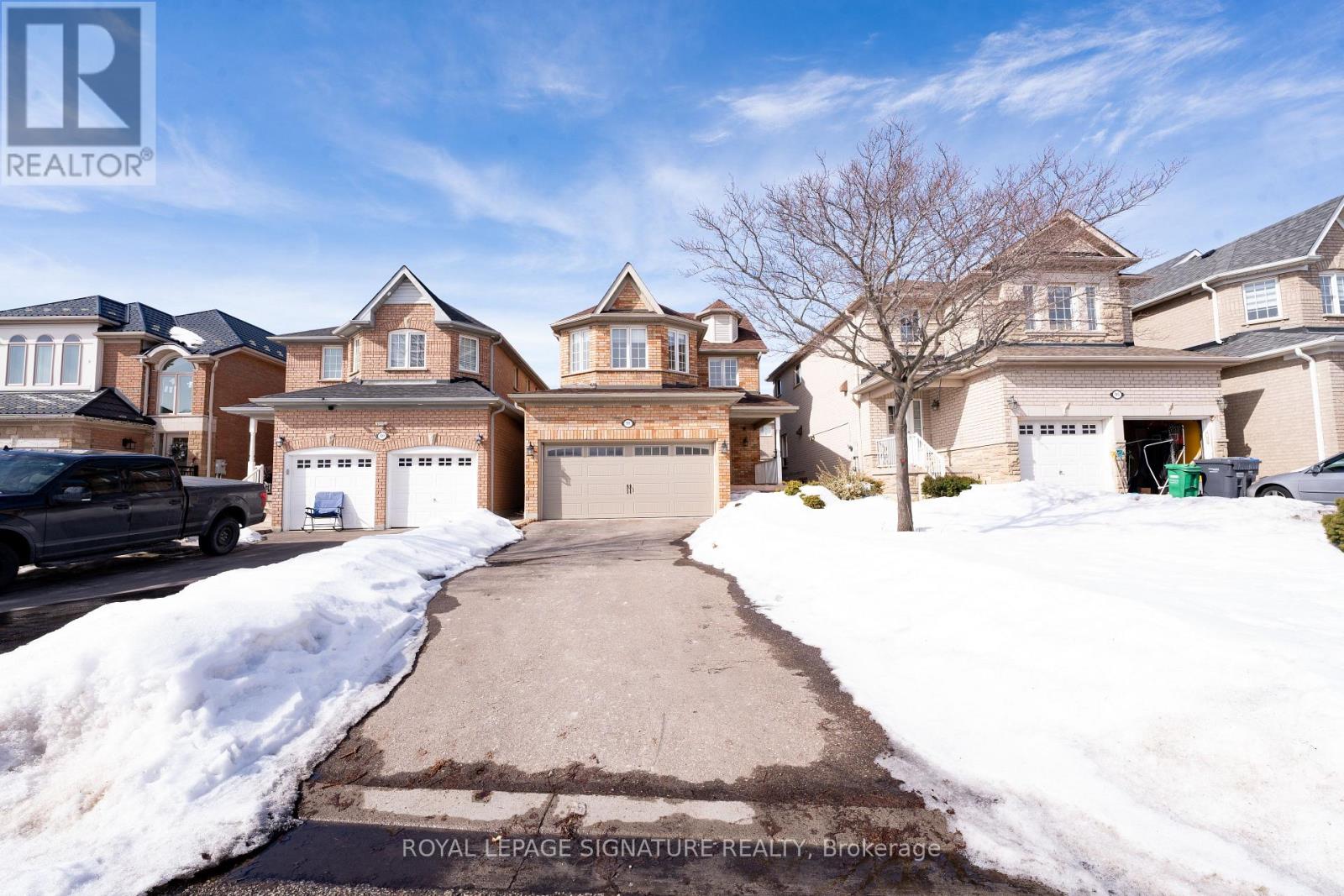 A snow-covered driveway leads to a row of houses with garages.