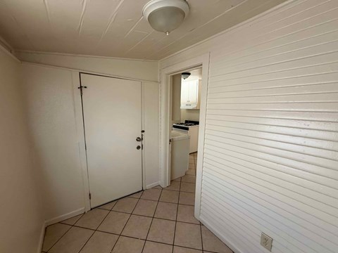 A white hallway with a door on the left and a kitchen area on the right.