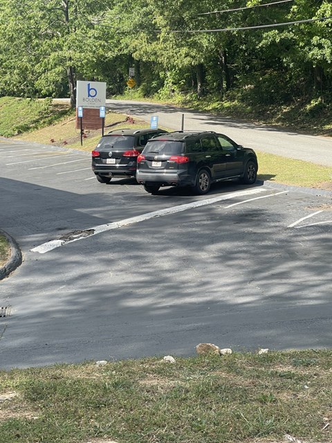 Two cars are parked in a parking lot with a sign that has a letter "b" on it.