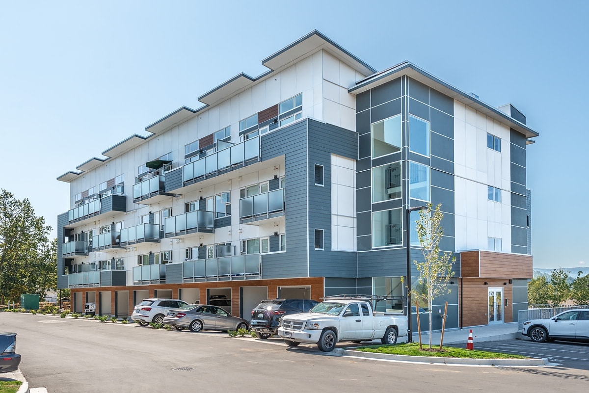 A modern multi-story apartment building with cars parked in front.