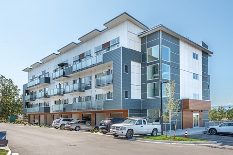 A modern multi-story apartment building with cars parked in front.