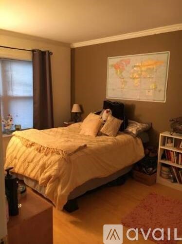 A bedroom with a bed, a lamp, a bookshelf, and a world map on the wall.