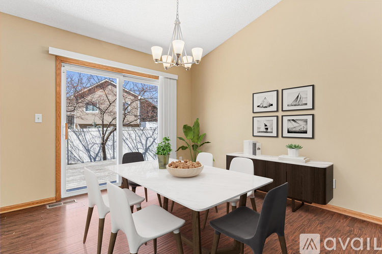 A dining room with a white table and chairs, a bowl of food, and a view of a house through a sliding glass door.