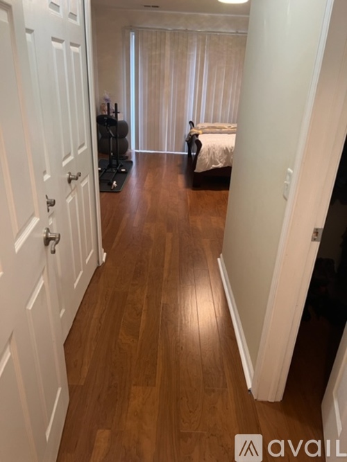 A hallway with a white door on the left and a bedroom with a bed and a person standing in the distance on the right.