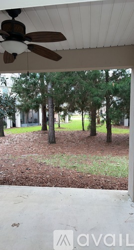 A patio with a ceiling fan and a view of a yard with trees.