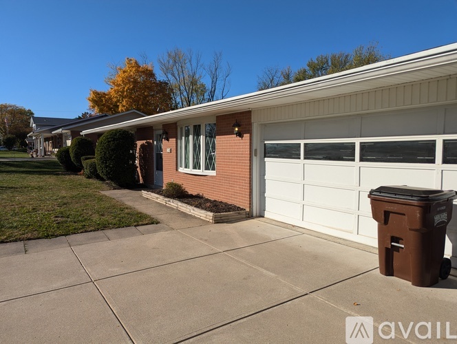 A brown trash bin sits on a driveway in front of a garage.