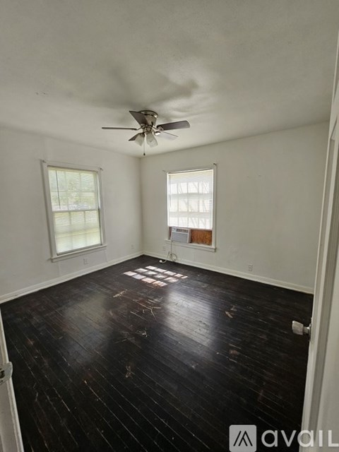 A room with a ceiling fan and two windows.