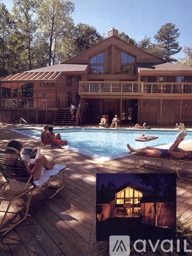 A large wooden house with a pool in front and people relaxing by the pool.