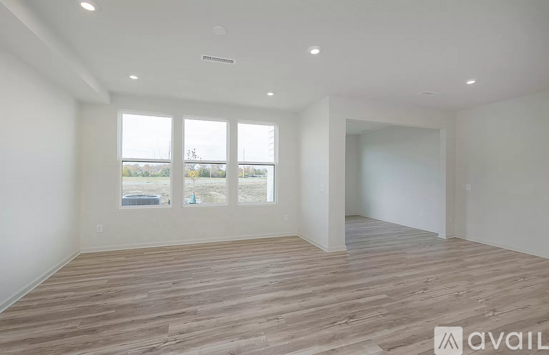 A spacious room with wooden flooring and large windows.