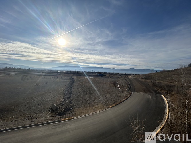 A winding road stretches into the distance under a clear blue sky with the sun shining brightly.