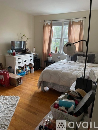A messy bedroom with a bed, dresser, and a window with curtains.