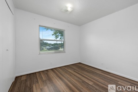 A room with wooden floors and a window showing a view of a car and trees.