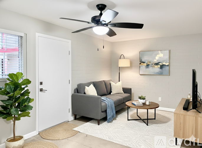 A living room with a grey couch, a ceiling fan, and a painting on the wall.