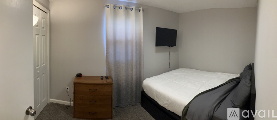 A small bedroom with a bed, dresser and window with curtains.