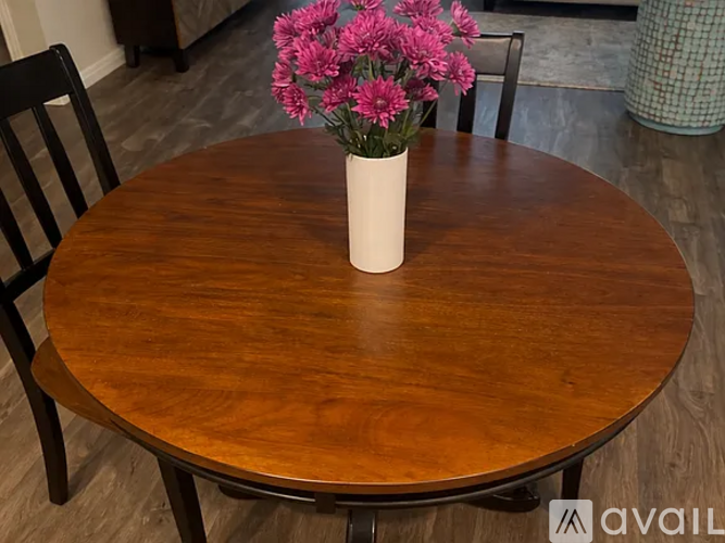 A wooden table with a vase of pink flowers on it.