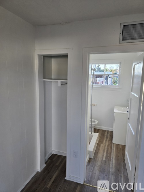 A white bathroom with wood flooring and a window.
