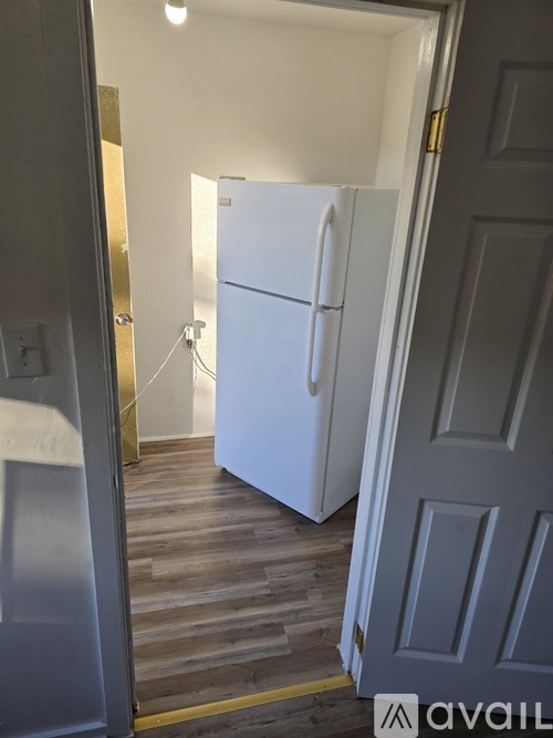 A white refrigerator is in a narrow hallway.