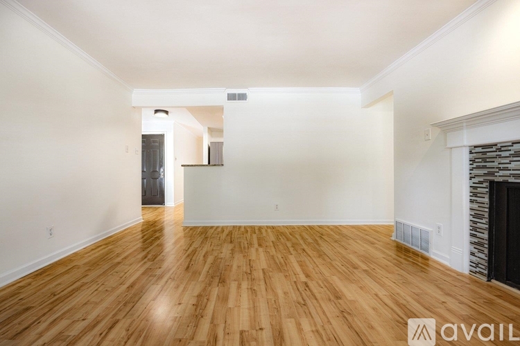 A spacious room with wooden flooring and a fireplace on the right side.
