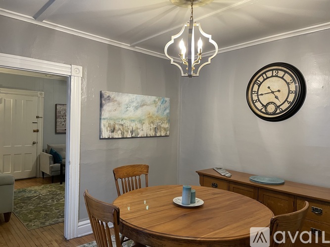 A dining room with a wooden table and chairs, a chandelier, and a large painting on the wall.