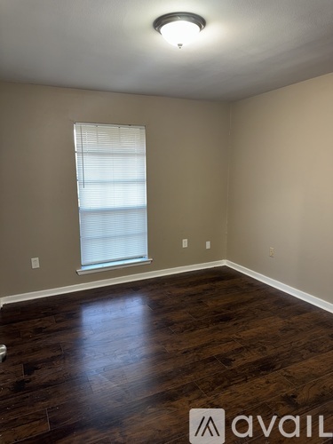 A room with wooden flooring and a window with blinds.