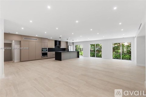 A spacious room with wooden flooring and a kitchen area with a counter and cabinets.