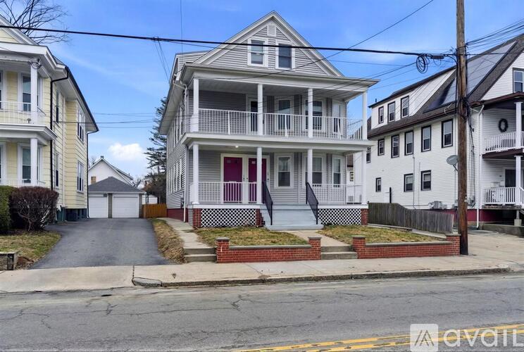 A two-story house with a red door and a balcony is in front of other houses.