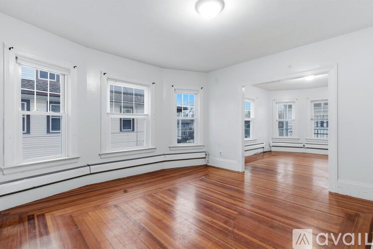 A room with wooden floors and white walls has windows with blinds.