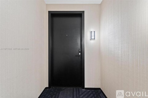 A black door is in a hallway with a wall sconce.