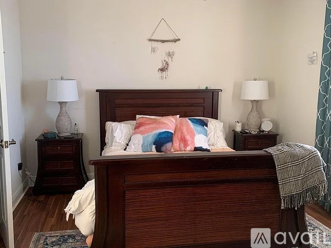A bedroom with a bed, two lamps, and a wall hanging.