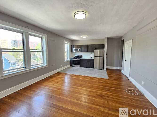 A spacious room with wooden flooring and a kitchen area with a refrigerator, microwave, and oven.