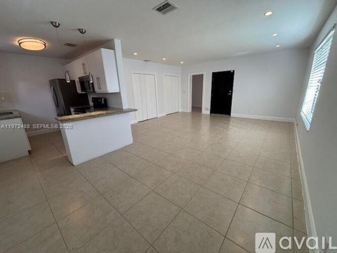 A spacious kitchen with white cabinets and a black refrigerator.
