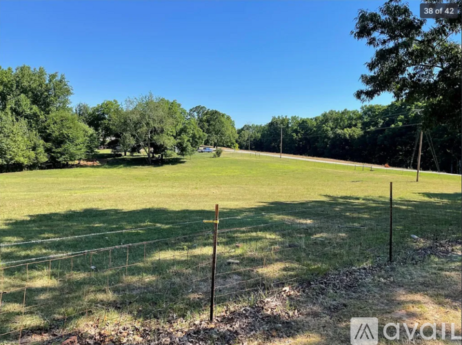 A grassy field with trees in the background and a fence running across the foreground.