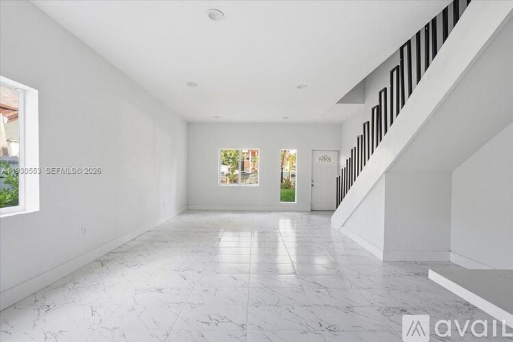 A spacious, white-walled room with a marble floor and a staircase on the right side.