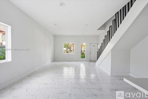 A spacious, white-walled room with a marble floor and a staircase on the right side.