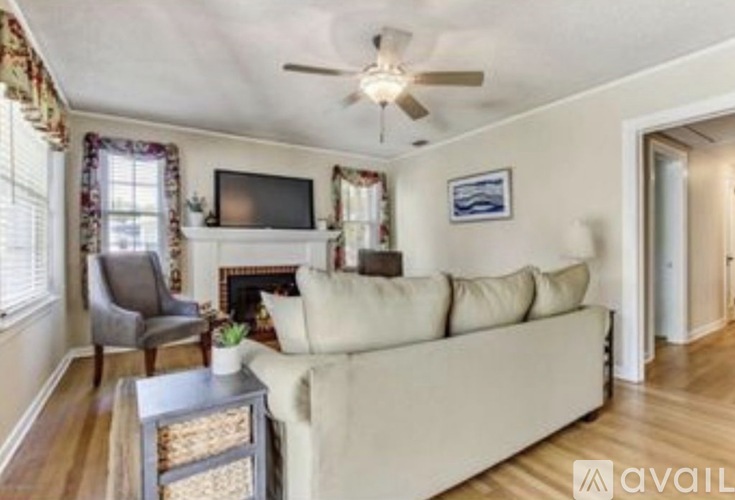 A living room with a beige couch, a television, a fireplace, and a ceiling fan.