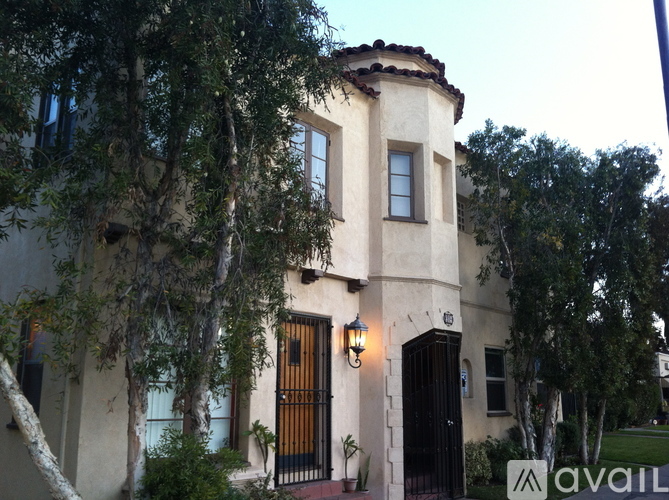 A house with a balcony and a black gate is surrounded by trees.