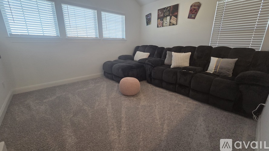 A living room with a grey carpet and a black sofa.
