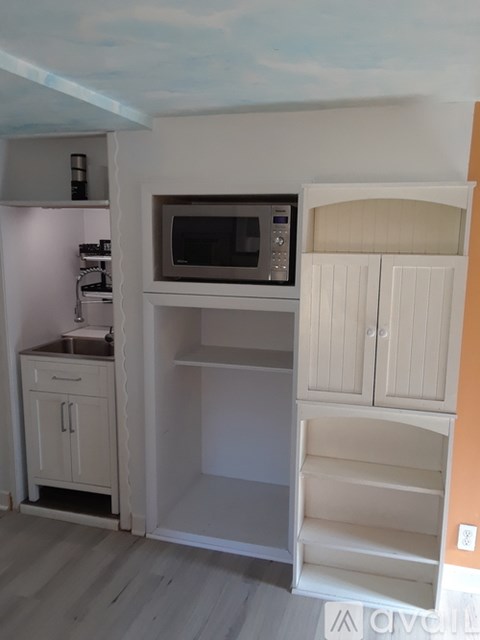 A kitchen with a microwave on top of a fridge and cabinets below.