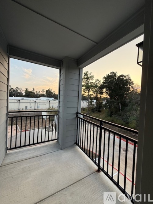 A balcony with a metal railing and a view of a parking lot and trees.