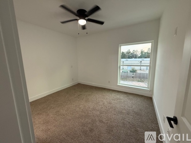 A room with a ceiling fan and a window overlooking a parking lot.