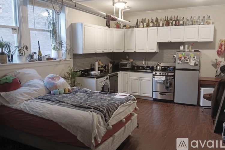 A bedroom with a bed, a kitchen, and a living area in a small apartment.