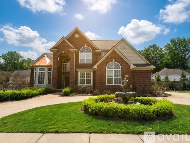 A house with a red brick exterior and a white trim is surrounded by a well-manicured lawn and a fountain in the front yard.