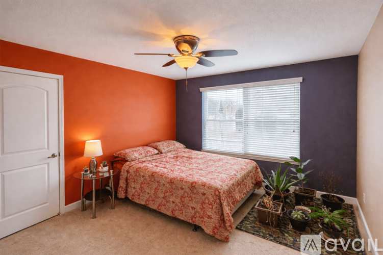 A bedroom with a bed, a table with a lamp, and a ceiling fan.