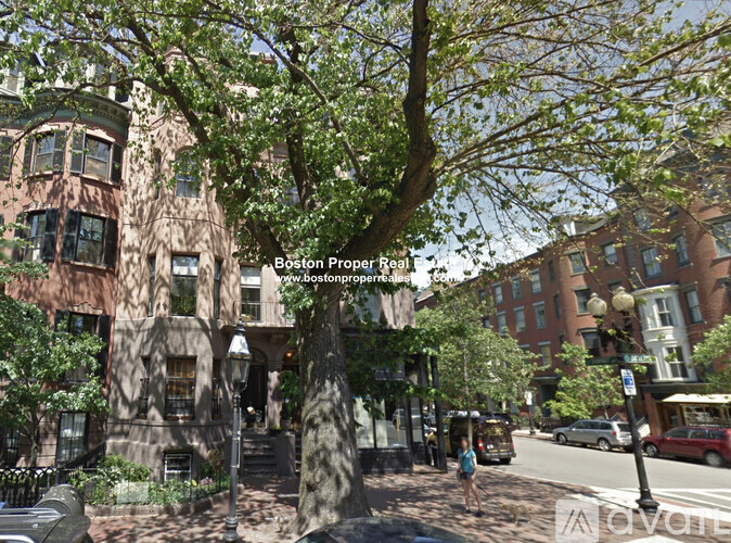 A tree in front of a building with a woman walking on the sidewalk.