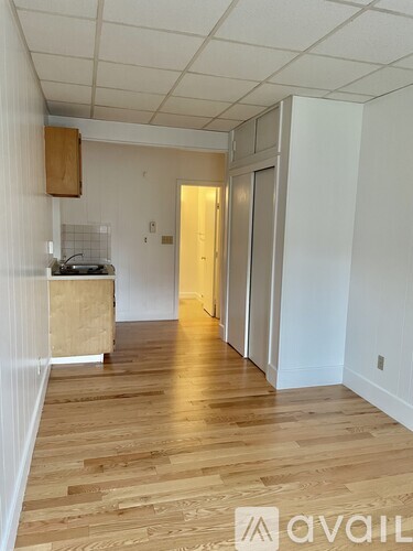A room with wooden floors and white walls, with a doorway leading to another room.