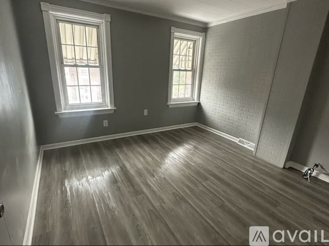 A room with wooden flooring and two windows.