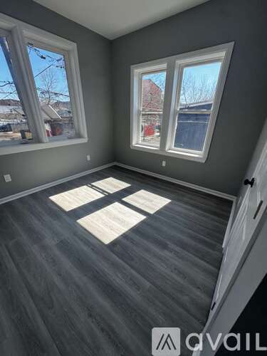 A room with grey walls and wooden flooring, with two windows and a door on the right side.