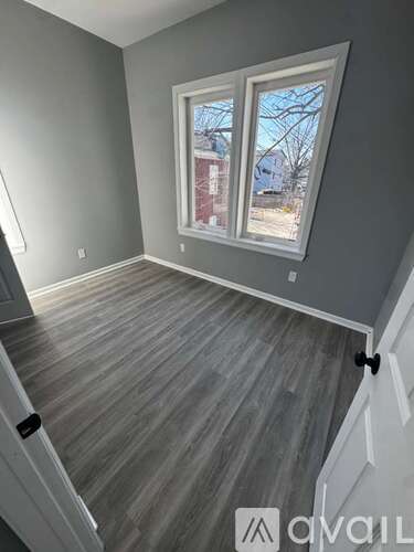 A room with grey walls and a window with a view of a red building outside.