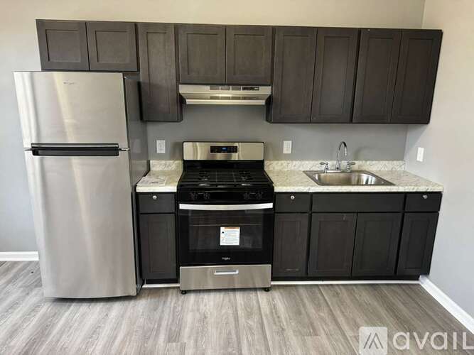 A kitchen with a stainless steel refrigerator, black cabinets, and a stove top oven.
